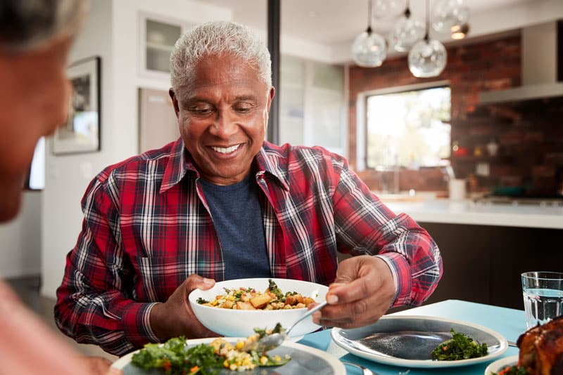 a dental implant patient smiling as he eats his soup because his periodontist told him how to avoid getting peri-implantitis.